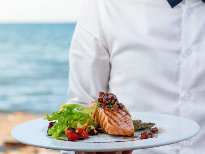 waiter holds a plate of grilled smoked salmon with lettuce, tomato, pepper